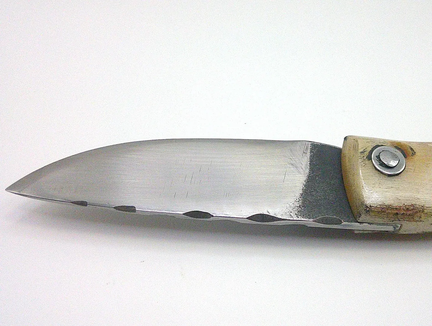 Détail de la lame en acier carbone XC75 du couteau corse artisanal Curnichjiolu Manu Padovani, avec finition brute près du manche.