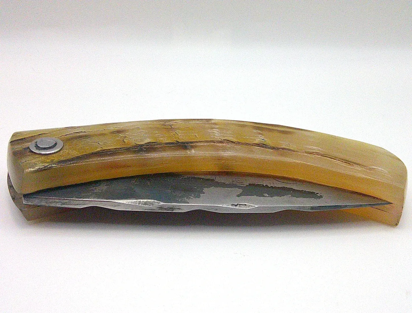 Couteau corse pliant Curnichjiolu Padovani fermé, manche en corne de bélier flammée aux nuances blondes et rousses, rivet apparent.