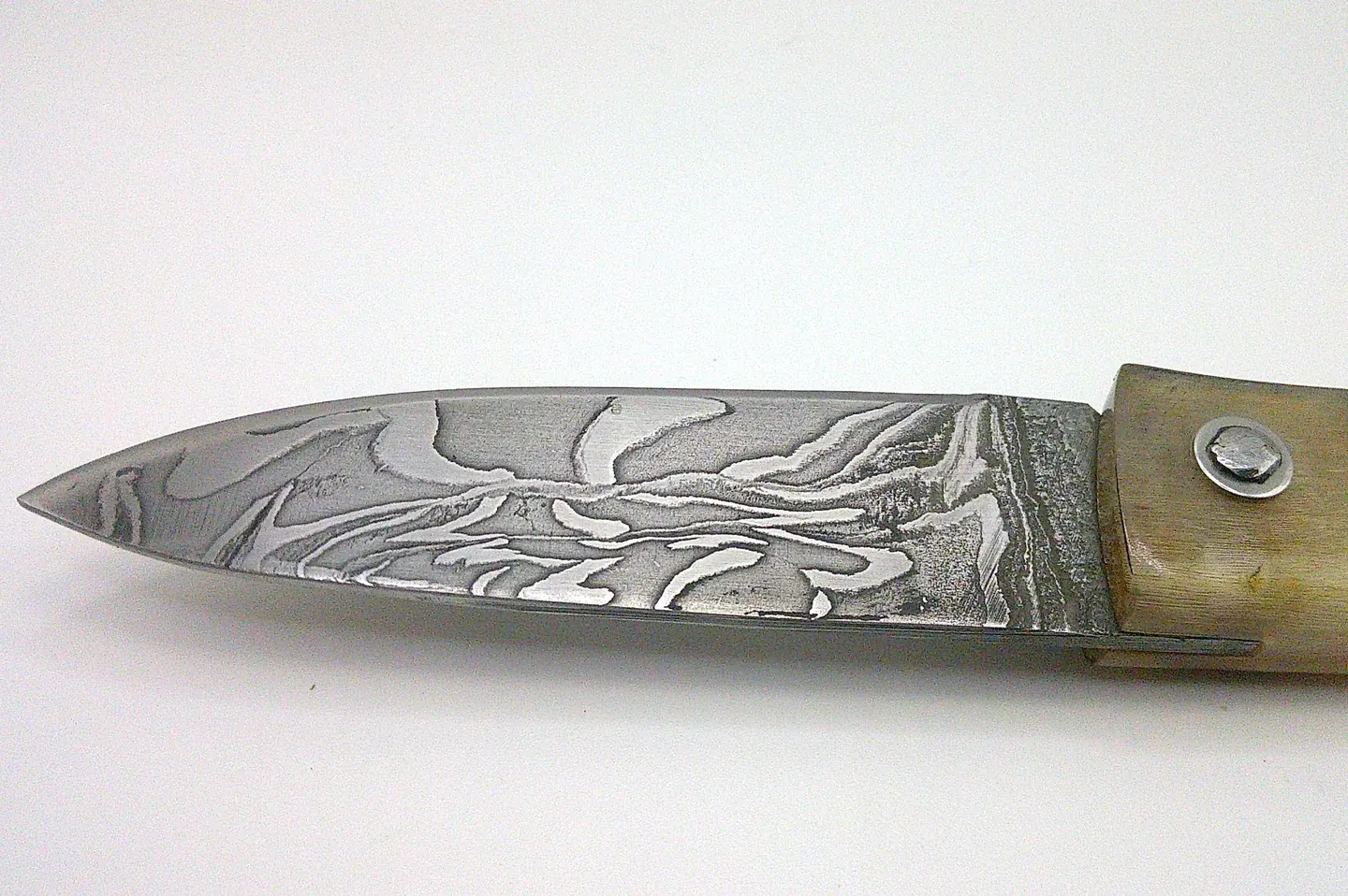 Gros plan sur les motifs ondulés de la lame en damas carbone du couteau corse artisanal Curnichjiolu Manu Padovani.